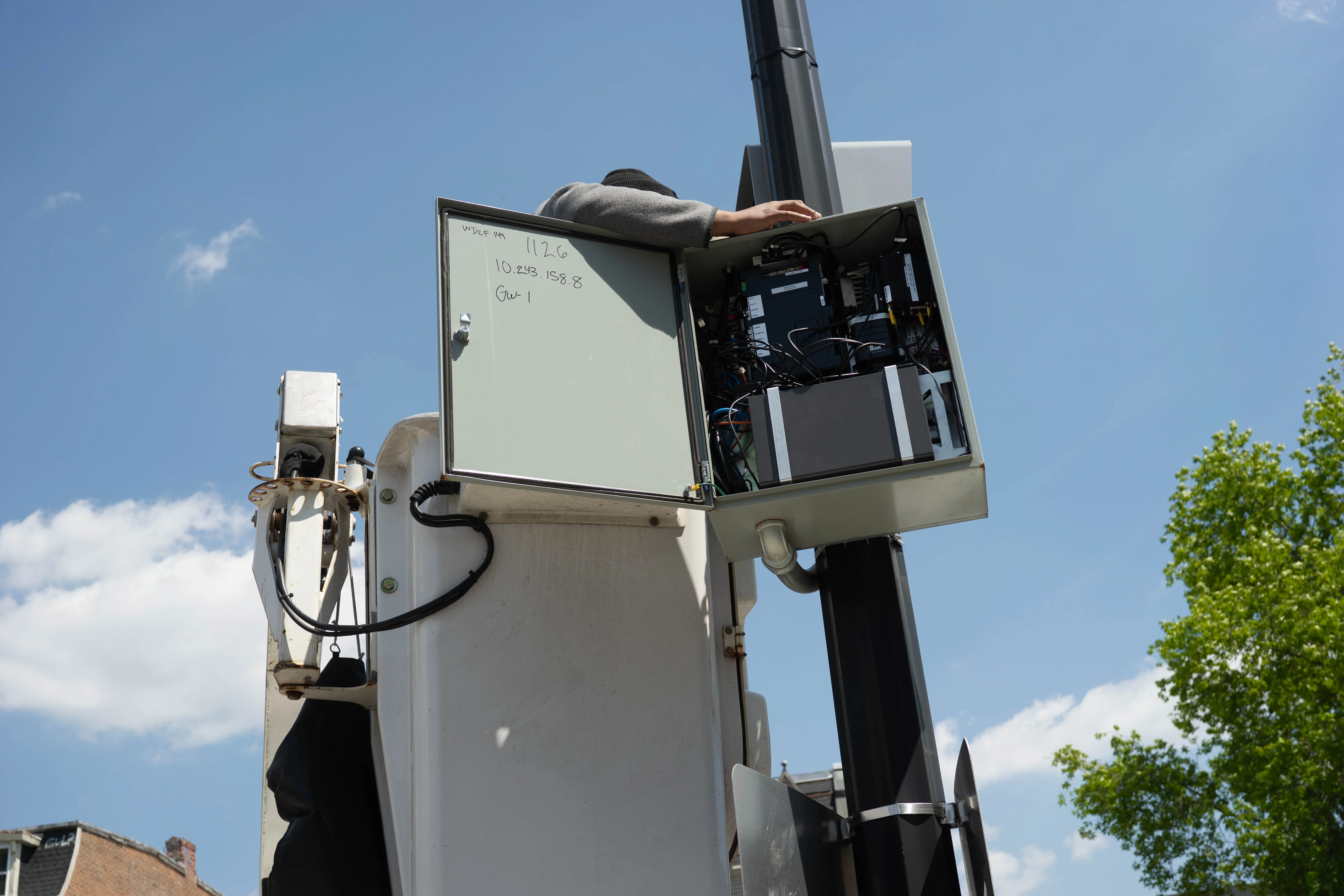 A person leans out of a raised press platform high on a hydraulic lift, working at equipment against a bright blue sky.